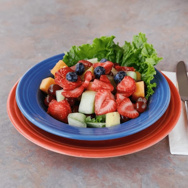Colorful fruit salad with strawberries, blueberries, melon, and grapes on lettuce in a blue bowl.